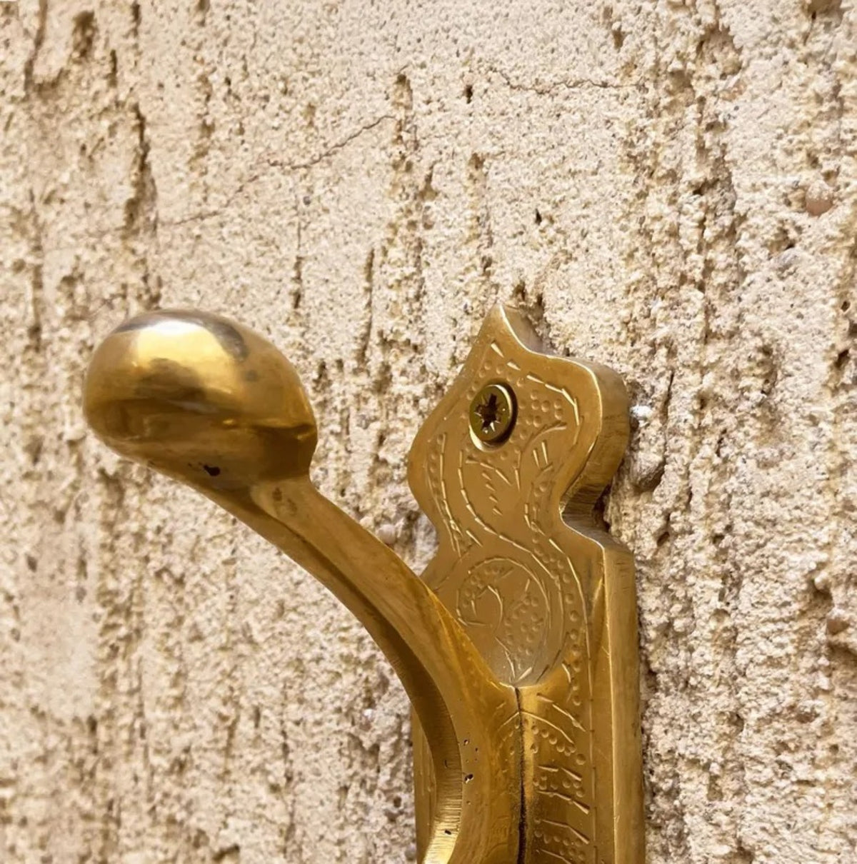Close-up of antique brass wall hook engraving and rounded tip