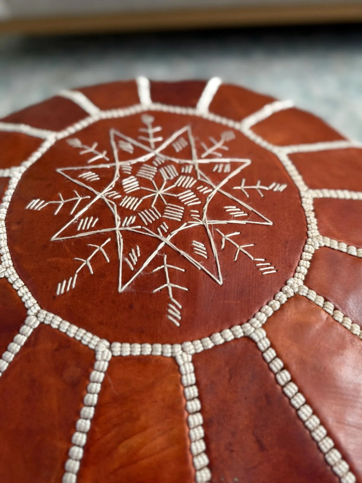 Close-up of white hand stitching and leather grain on a cognac Moroccan pouf