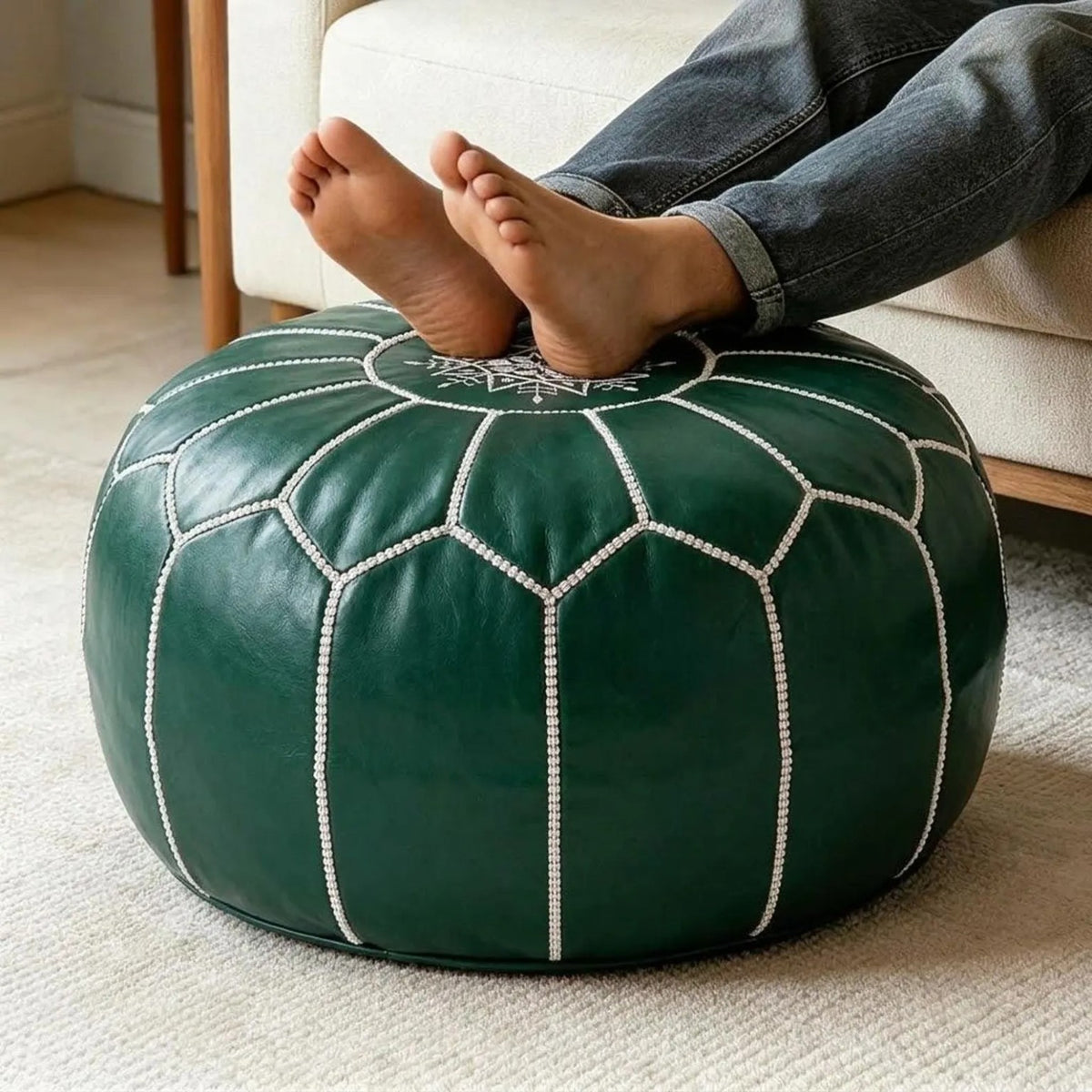Person relaxing with feet resting on an emerald green Moroccan leather pouf
