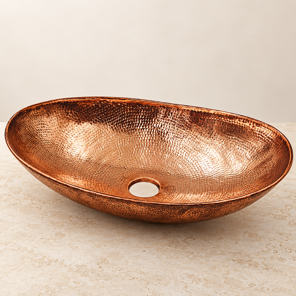 Handcrafted oval hammered copper vessel sink on an ivory studio background