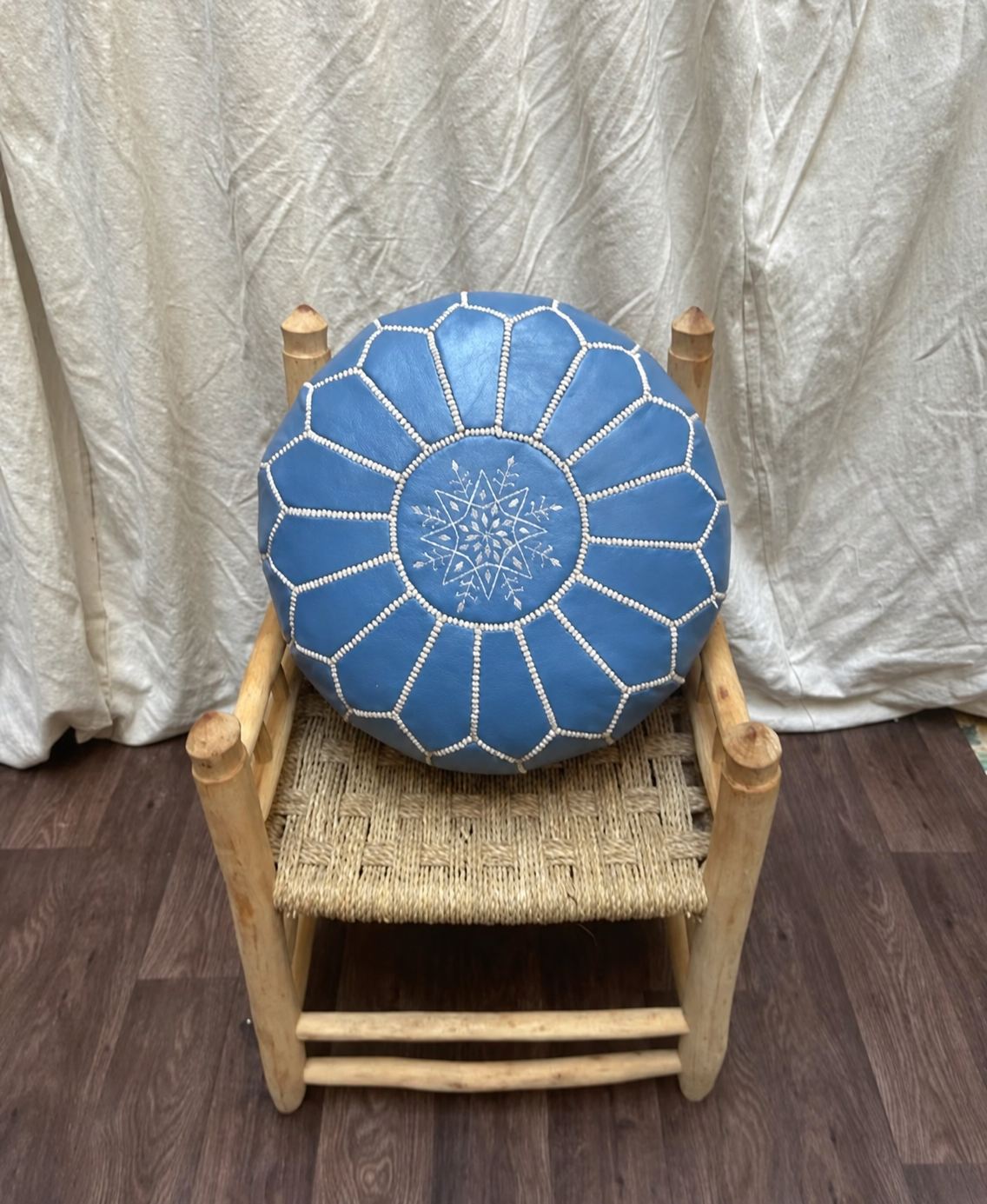 Sky blue Moroccan leather pouf displayed on a handcrafted wooden chair